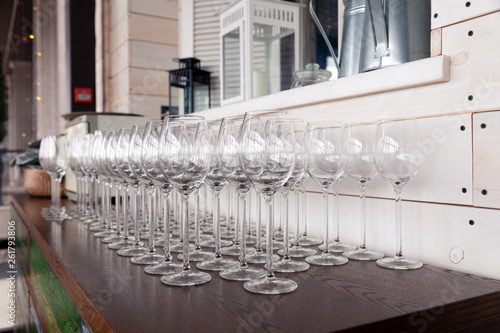 Many transparent crystal wine glasses stand in row on the brown wooden shelves of the rack. Side view. Concept of tasting, banquet, catering, buffet, lunch, anniversary, wedding, birthday