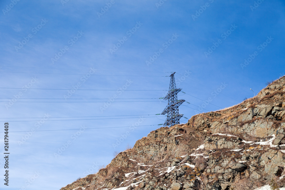 High voltage post transmission power line, electricity distribution station on the mountain with stones on th background of blue sky