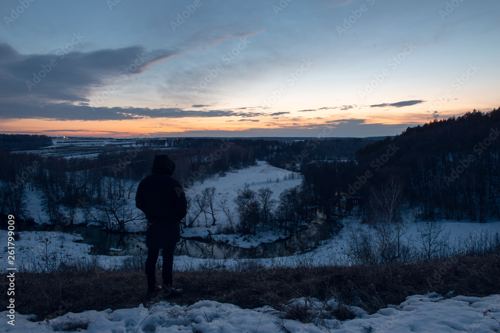 Obraz premium Man stands on a hill against the background of the river and sunset