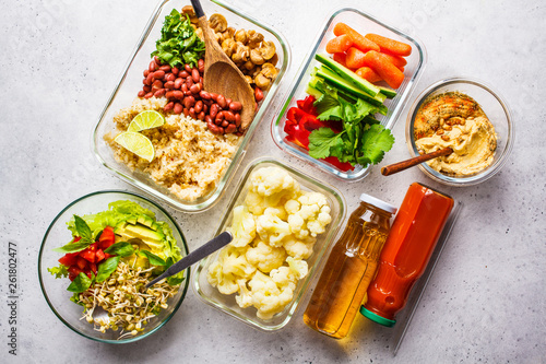 Healthy vegan food in glass containers, top view. Rice, beans, vegetables, hummus and juice.