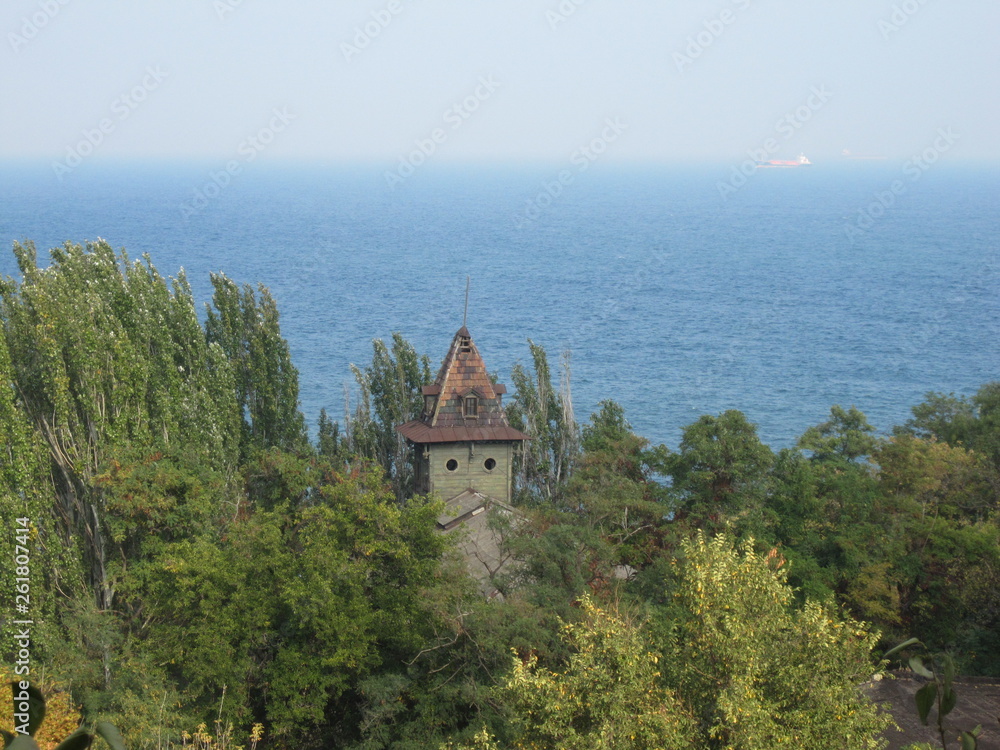 old damaged tower of a villa in a forest in front of the black sea with a container ship in the background near the harbour of odessa
