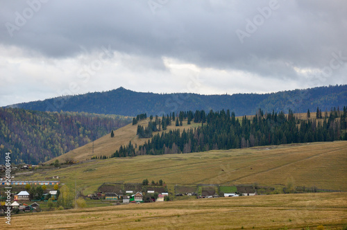Heavy grey clouds in the cold autumn sky over village with small houses far away in the mountains and fields. Travelling. People living