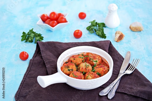 Fish meatballs in tomato sauce in a white ceramic pan on a light blue concrete background.
