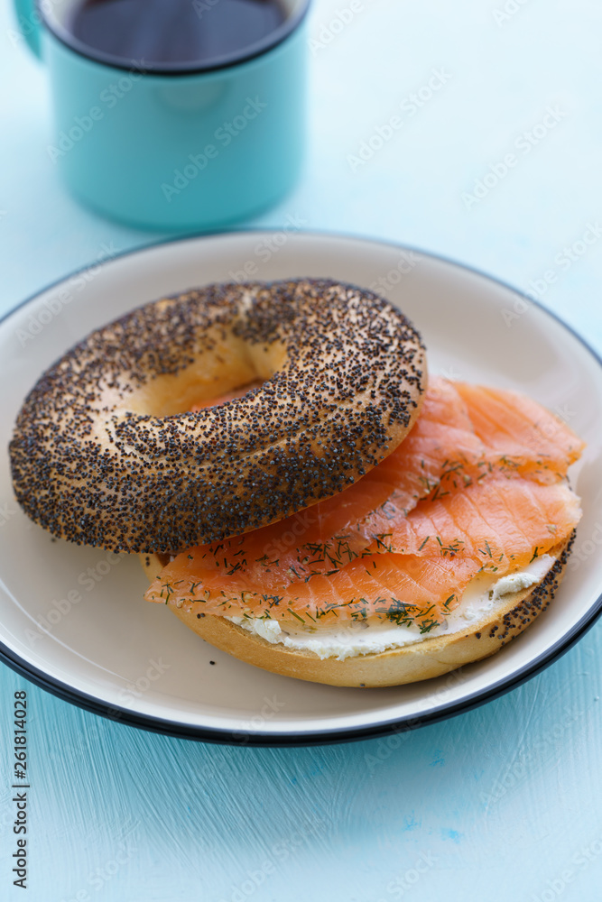 Poppy seeds bagel with cream cheese and smoked salmon served on a white plate with black rim. Blue table, high resolution
