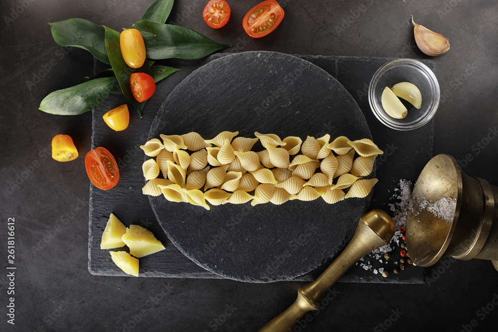 Pasta shells on black stone. Tomatoes and bay leaves with allspice and sea salt.