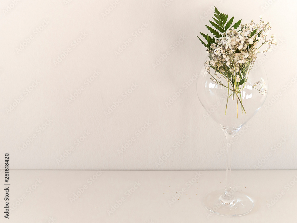 The border of delicate little white flowers on white background from front. Flat lay style. Space for text. Gypsophila on glass with leaf of fern