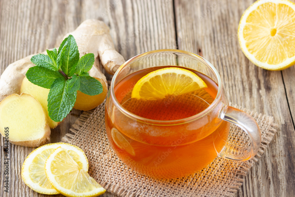 A glass cup of tea with lemon, mint and ginger on wooden rustic table. A glass cup of tea with lemon, mint and ginger on wooden rustic table.