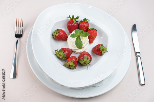 a ball of white ice cream with strawberries and mint on a white plate