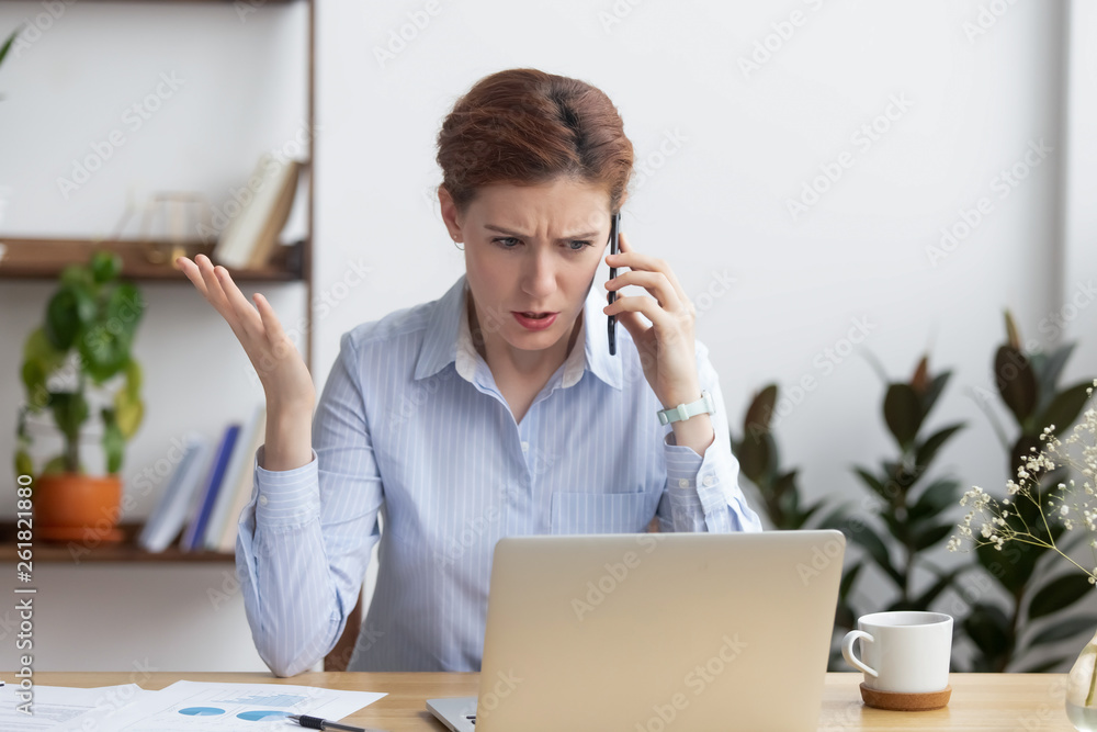 Angry mad businesswoman talking on phone looking at laptop Angry mad businesswoman talking on phone looking at laptop