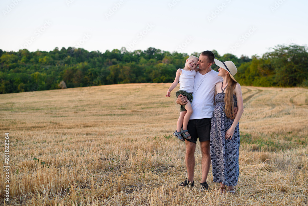 Happy young family. A father with a little son in her arms and a pregnant mother. Beveled wheat field on the background. Sunset time.