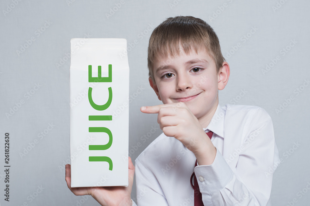 Little blond boy holds and shows the index finger on a large white carton juice package. White shirt and red tie. Light background Little blond boy holds and shows the index finger on a large white carton juice package. White shirt and red tie. Light background