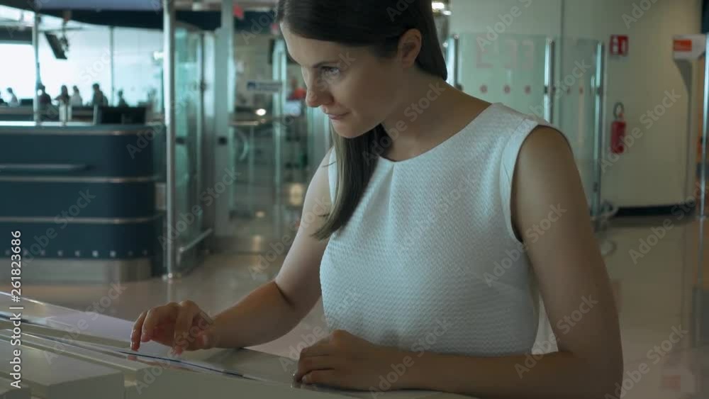 Woman in white blouse in airport terminal using touchscreen to check departures. Female tourist looking for her flight online Woman in white blouse in airport terminal using touchscreen to check departures. Female tourist looking for her flight online