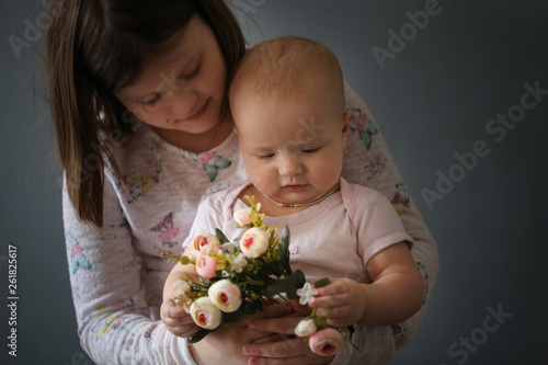 Kid girl hugging baby and holding together flowers