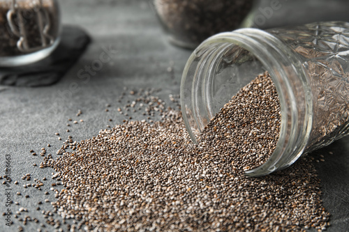 Glass jar and scattered chia seeds on grey table, closeup. Space for text