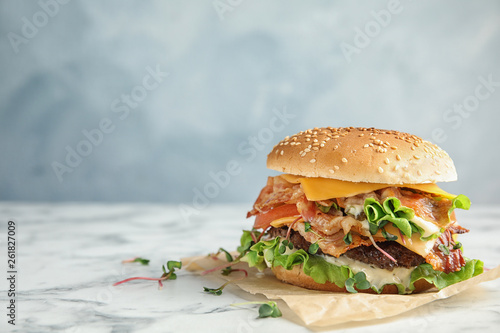 Tasty burger with bacon on table against color background. Space for text