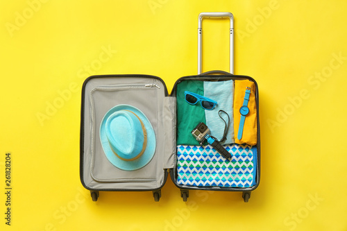 Open suitcase with summer clothes and accessories on color background, top view photo