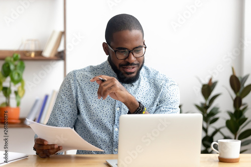 Focused african american businessman working with laptop documents in office photo