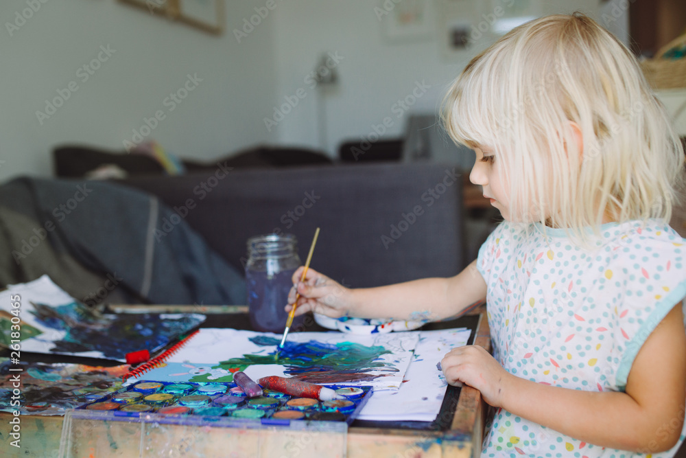 Little cute blonde girl painting at home