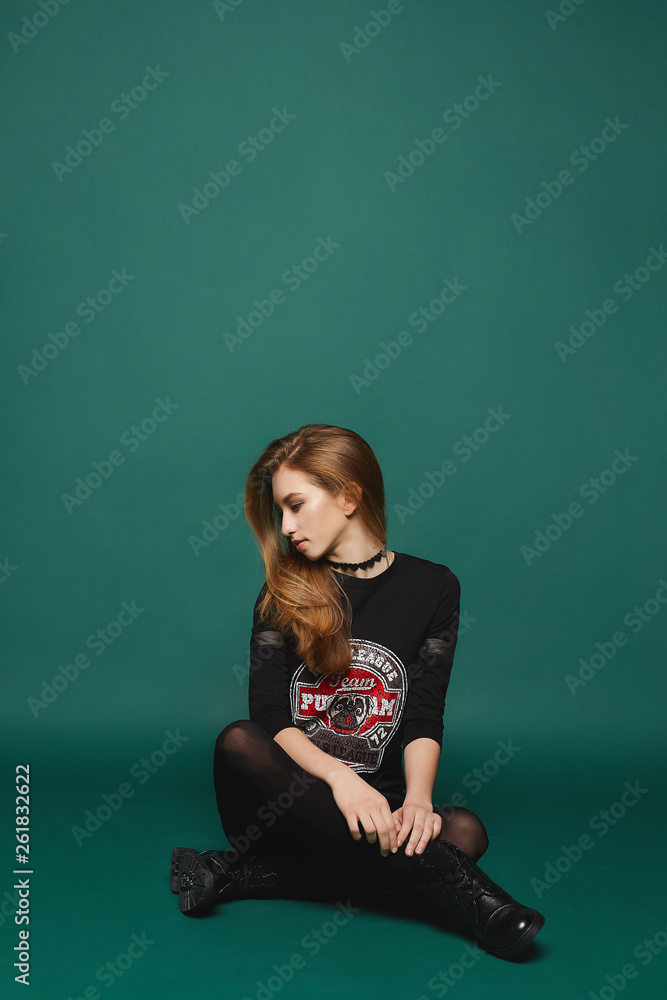 Stylish and beautiful young model girl in black fashionable dress and boots isolated over dark-green background in studio Stylish and beautiful young model girl in black fashionable dress and boots isolated over dark-green background in studio