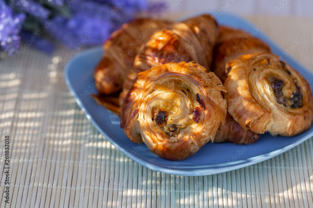 Buns with raisins and french croissants on a blue plate. Dessert. Lavender flowers. Dinner in a garden in summertime. Soft focus. Blurry background. Close-up. Macro. Buns with raisins and french croissants on a blue plate. Dessert. Lavender flowers. Dinner in a garden in summertime. Soft focus. Blurry background. Close-up. Macro.