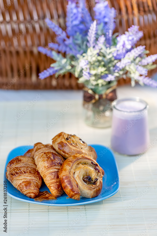 French croissants, buns with raisins and blueberry yogurt in a glass jar on a table. Summertime. Bouquet of flowers lavender. Dessert. Soft focus. Blurry background. French croissants, buns with raisins and blueberry yogurt in a glass jar on a table. Summertime. Bouquet of flowers lavender. Dessert. Soft focus. Blurry background.