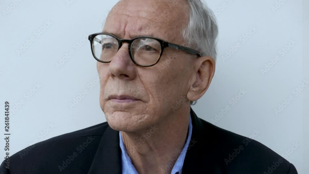 Senior citizen puts on glasses in front of white backdrop. Senior citizen puts on glasses in front of white backdrop.