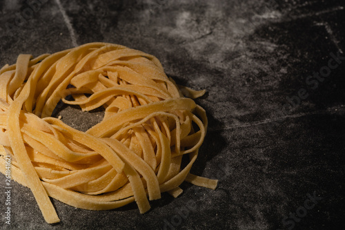 Isolated raw pasta on a black background with a place for text. Traditional Italian pasta, noodles, tagliatelle. Top view. Copy space. photo