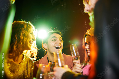Positive emotional young friends laughing and chatting while drinking champagne and having fun at party in nightclub
