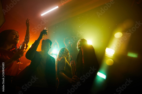 Group of carefree young multiethnic people dancing in disco lights and drinking alcohol at night party