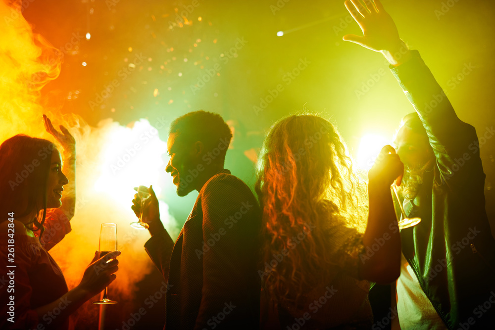Fototapeta premium Happy excited young people dancing in smoke and drinking champagne while talking and enjoying party time