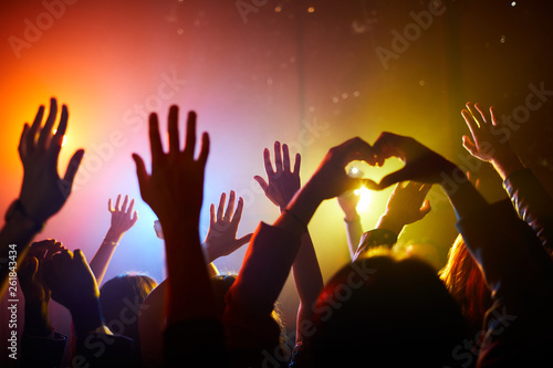 Crowd of unrecognizable fans waving hands and enjoying performance at concert, man making heart gesture