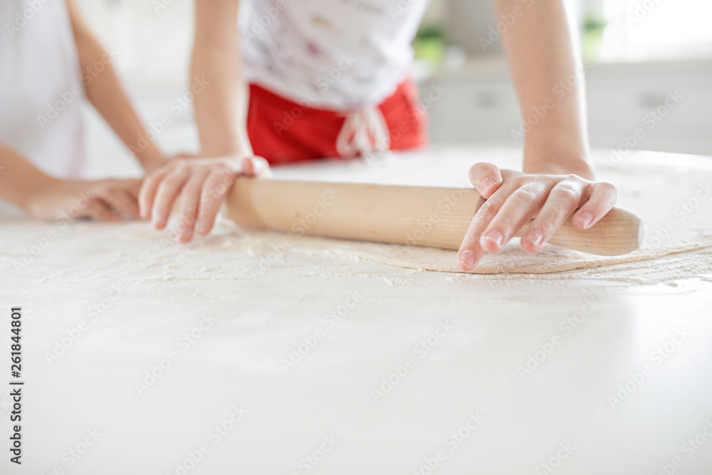 Children's hands roll out the pizza dough on a white table. Having fun together in the kitchen. View from above.