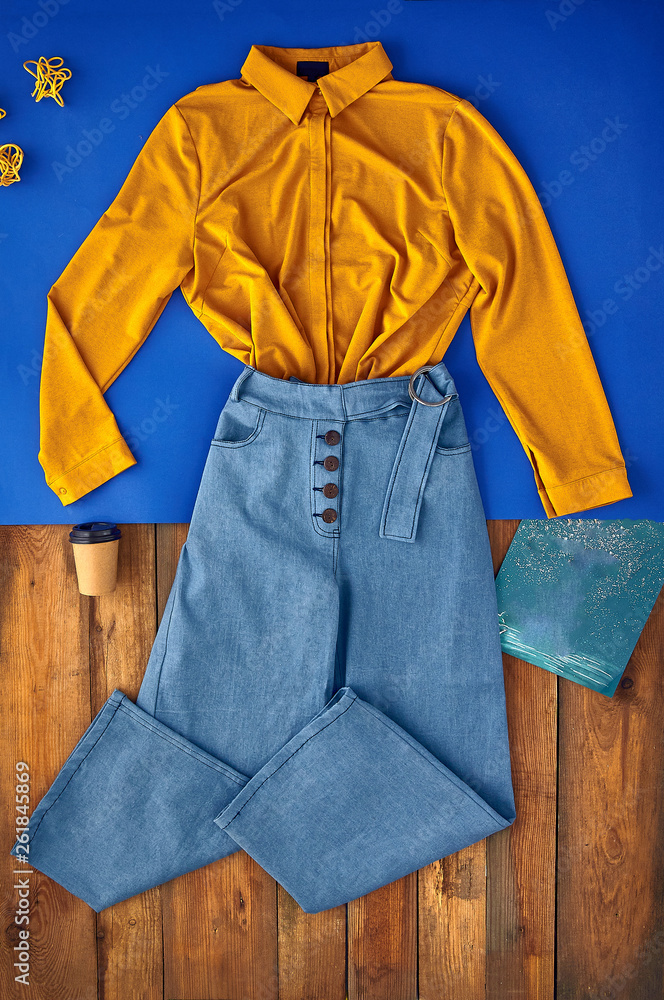 Beautiful unusual outfit presentation for fashion blog, advertising,  clothing catalog. Yellow, mustard business shirt and unusual wide jeans  with a belt. Work outfit and paper cup for coffee. Photos | Adobe Stock