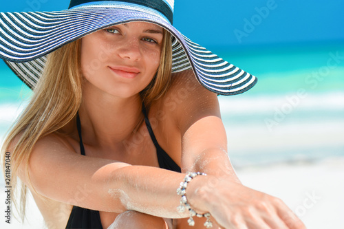 Fit smiling girl on a tropical beach with hat. Sexy woman with hat on paradise tropical beach. Beautiful fit body girl on travel vacation. Banner crop for copy space.