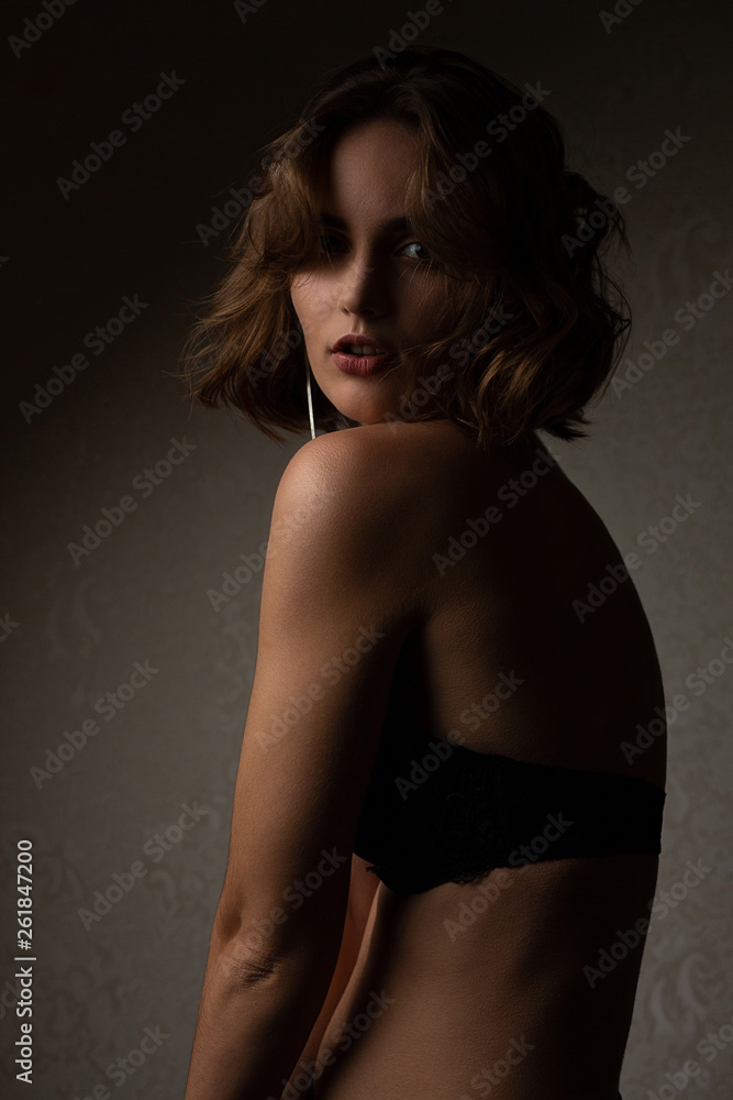 Glamor brunette girl with curly hair wearing bra posing with contrast light