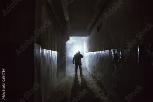 Silhouette of man in standing in dark scary corridor or tunnel with back light