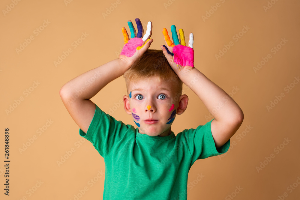 Cheerful modern boy with hands painted in colorful paints ready for hand prints. he poses on a beige background - Image Cheerful modern boy with hands painted in colorful paints ready for hand prints. he poses on a beige background - Image