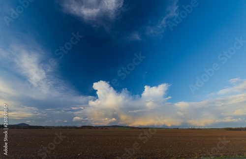 Landscape with plowed field and dynamic clouds on a blue sky by sunset