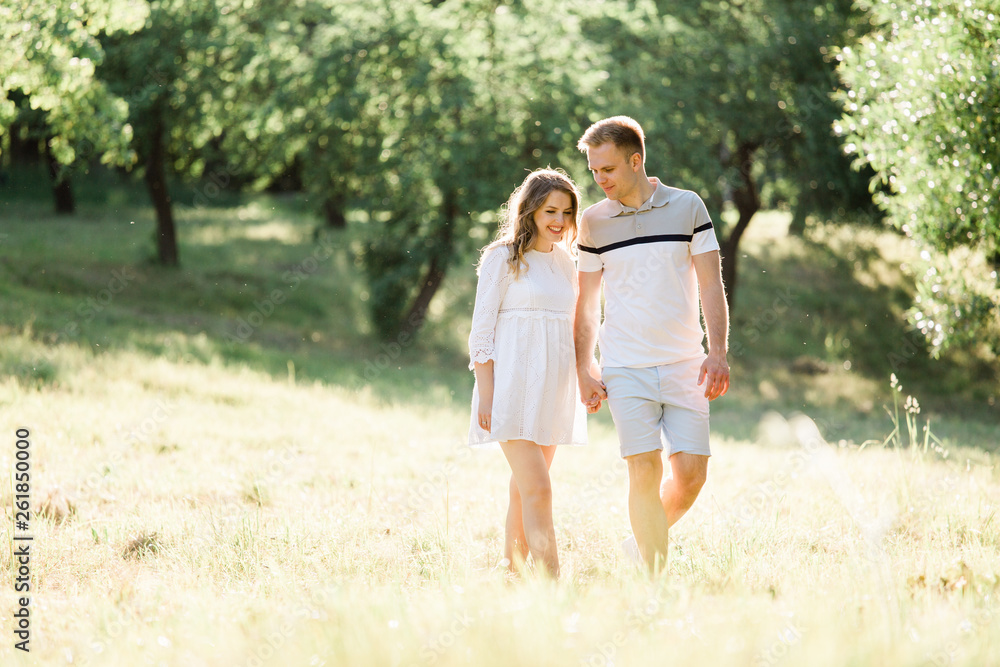 Young pretty couple in love walking  in park. Handsome cheerful blonde girl in white dress hugging her boyfriend. Man and woman having fun outdoors