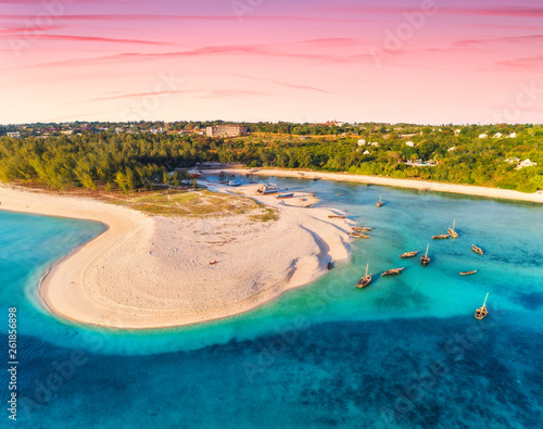 Aerial view of the fishing boats on tropical sea coast with sandy beach at sunset. Summer holiday. Indian Ocean, Zanzibar, Africa. Landscape with boat, green trees, blue water, colorful sky. Top view