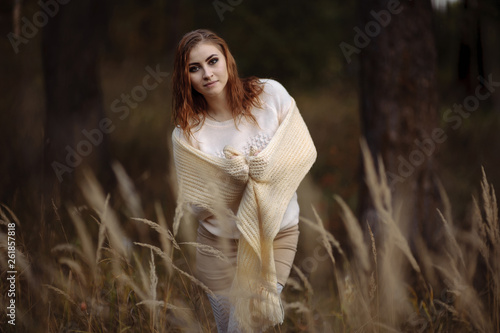 red-haired girl in bright clothes on a background of autumn forest and yellow ears on a sunny day