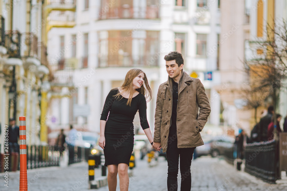 Urban modern young love couple walking romantic talking talking, holding hands on a date. Young multicultural Turkish brunette and Caucasian couple on old european street. Autumn spring weather