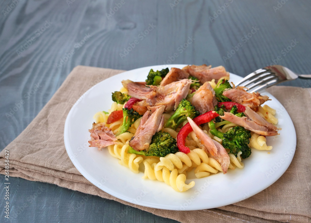 Fusilli pasta with pulled chicken meat, broccoli and vegetables on white plate over wooden table Fusilli pasta with pulled chicken meat, broccoli and vegetables on white plate over wooden table