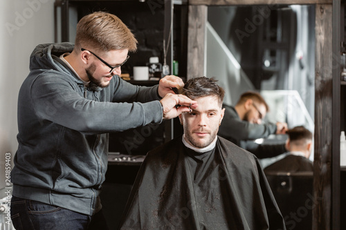Hair cutting with metal scissors. Master cuts hair and beard of men in the barbershop, hairdresser makes hairstyle for a young man