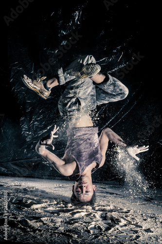 cool dirty japanese guy dancer in style bboying doing complex tricks on floor in Studio filled with flour on black background. concept of space dance on surface of planet moon. toned sepia, instagram