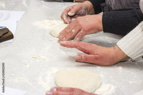 Baking concept. Hard working women prepares pastry by himself, kneads dough on wooden counter with flour and rolling pin. Women cook bakes bread or delicious bun or pasta