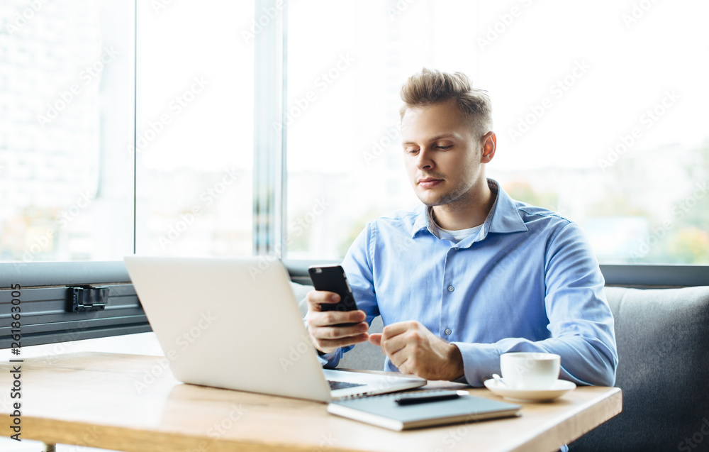 Young handsome man sitting in office with cup of coffee and working on project connected with modern cyber technologies. Businessman with notebook trying to keep deadline in digital marketing sphere. Young handsome man sitting in office with cup of coffee and working on project connected with modern cyber technologies. Businessman with notebook trying to keep deadline in digital marketing sphere.