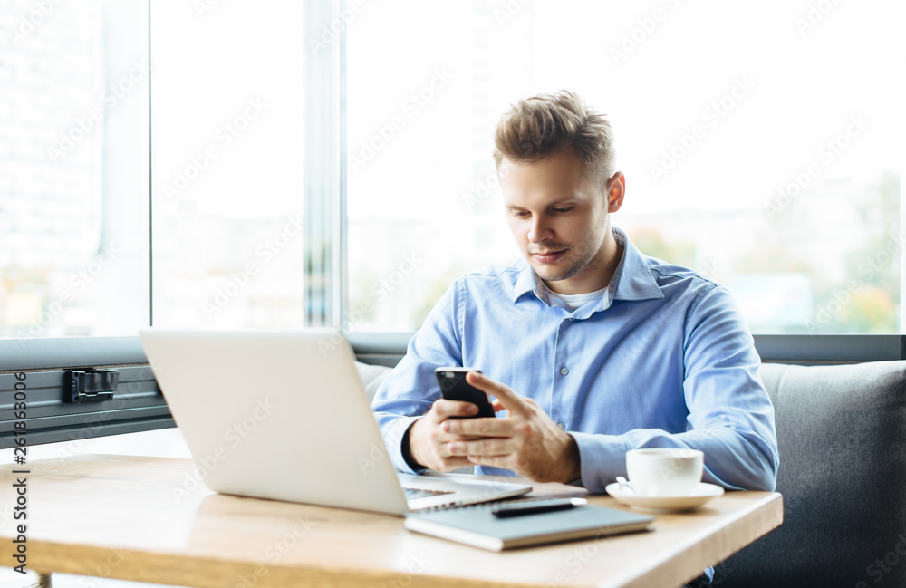 Young handsome man sitting in office with cup of coffee and working on project connected with modern cyber technologies. Businessman with notebook trying to keep deadline in digital marketing sphere. Young handsome man sitting in office with cup of coffee and working on project connected with modern cyber technologies. Businessman with notebook trying to keep deadline in digital marketing sphere.