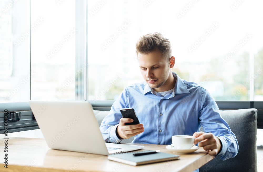 Young handsome man sitting in office with cup of coffee and working on project connected with modern cyber technologies. Businessman with notebook trying to keep deadline in digital marketing sphere. Young handsome man sitting in office with cup of coffee and working on project connected with modern cyber technologies. Businessman with notebook trying to keep deadline in digital marketing sphere.