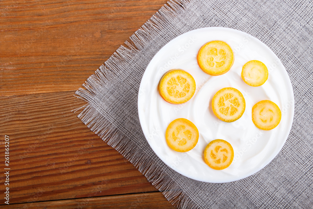 greek yogurt with kumquat pieces in a white plate on a brown wooden background greek yogurt with kumquat pieces in a white plate on a brown wooden background